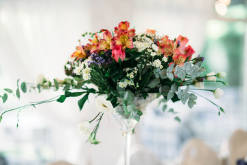Tall glass vase with orange flowers stands in the room