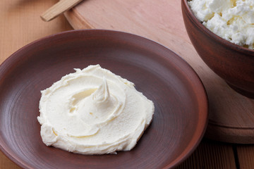 Cheese, cottage cheese and cream in clay ware, fresh curd on a wooden background, rustic sour cream, brown shade, healthy food, French breakfast, top view, goat curd, protein