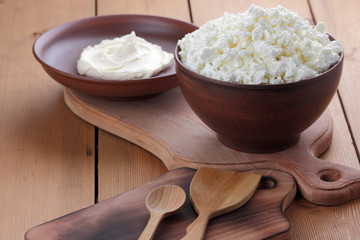 Cheese, cottage cheese and cream in clay ware, fresh curd on a wooden background, rustic sour cream, brown shade, healthy food, French breakfast, top view, goat curd, protein