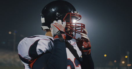 American Football Player Putting On Helmet on large stadium with lights in background