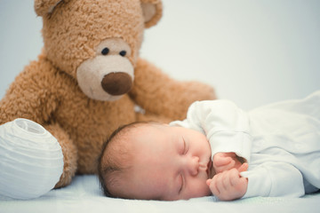 newborn baby laying with teddy bear on blanket