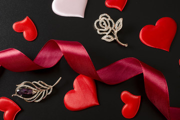 Composition with brooches, hearts and ribbon on a black background