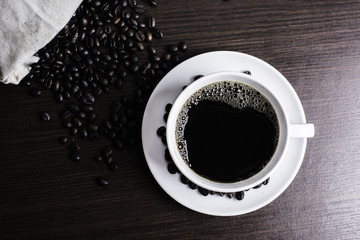 Black coffee in white cup and coffee bean on wood table background.