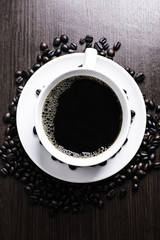 Black coffee in white cup and coffee bean on wood table background.
