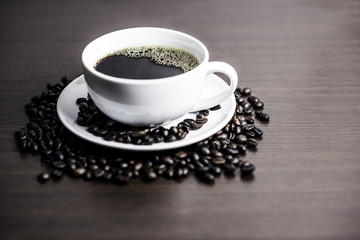 Black coffee in white cup and coffee bean on wood table background.
