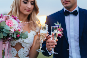 Bride and groom clang glasses with champagne standing on the field