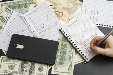 notepad with growth chart, hand with pen, money and cellphone