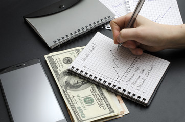 notepad with growth chart, hand with pen, money and cellphone