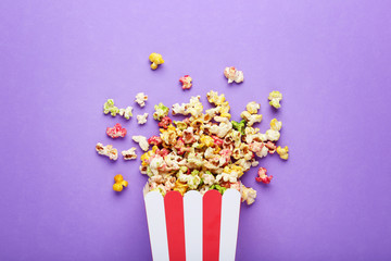 Sweet popcorn in striped bucket on purple background