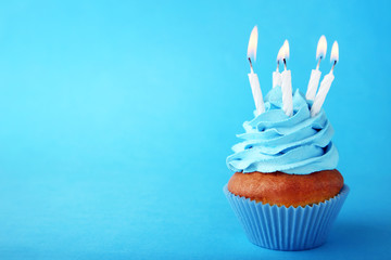 Tasty cupcake with candles on blue background