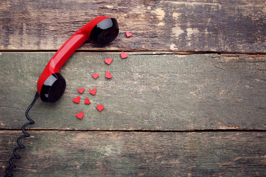 Telephone handset with red hearts on wooden table