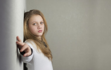 Portrait of sad blond teen girl standing near wall