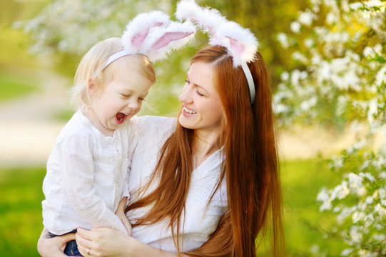 Young mother and her daughter wearing bunny ears in a spring garden on Easter day