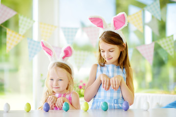 Two cute little sisters wearing bunny ears playing egg hunt on Easter