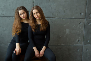 portrait of two beautiful young girls of twin sisters with flowing hair against the gray wall in the interior