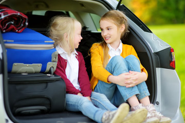 Two adorable little girls sitting in a car before going on vacations with their parents. Two kids looking forward for a road trip or travel.