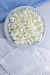 Cheese, cottage cheese on a white plate, fresh cottage cheese on a white and blue napkin, dairy product on a white background, healthy food, French breakfast, top view, goat curd in minimalist style, 