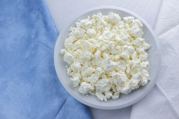 Cheese, cottage cheese on a white plate, fresh cottage cheese on a white and blue napkin, dairy product on a white background, healthy food, French breakfast, top view, goat curd in minimalist style, 