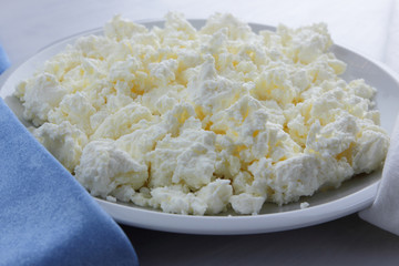 Cheese, cottage cheese on a white plate, fresh cottage cheese on a white and blue napkin, dairy product on a white background, healthy food, French breakfast, top view, goat curd in minimalist style, 