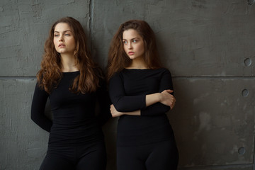 portrait of two beautiful young girls of twin sisters with flowing hair against the gray wall in...