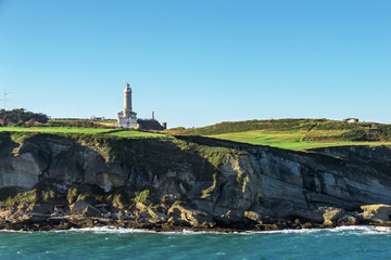 Beautiful natural coast scene containing lighthouse at green environment in front of water