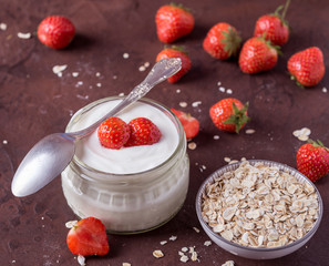 White yogurt in glass bowl with spoon and starwberries on rustic background.