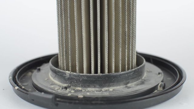 Tilt up footage of a dirty vacuum cleaner filter, full of dust and dirt, on white background.