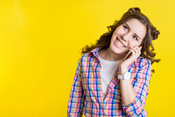 Fototapeta premium A teenage girl speaks on the phone with a smile on her face. Yellow background for text