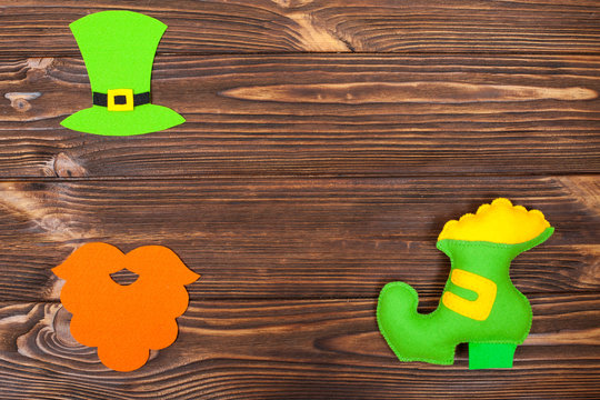 St. Patrick's Day theme colorful horizontal banner. Green leprechaun hat, beard and shoe with gold on brown wooden background. Felt craft elements. Copy space. For greeting card,congratulation banner