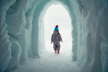 little girl is exploring the ice cave in a winter park