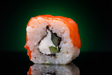 One roll with red fish and cucumber on a black background. Japanese restaurant menu, close-up