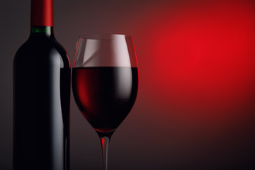  Bottle of red wine with a glass against a dark background and space for text