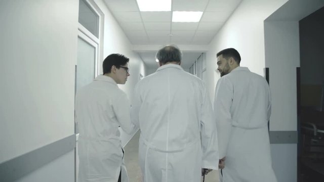 Three male doctors discuss a patient's notes when walk in hospital corridor. 4K