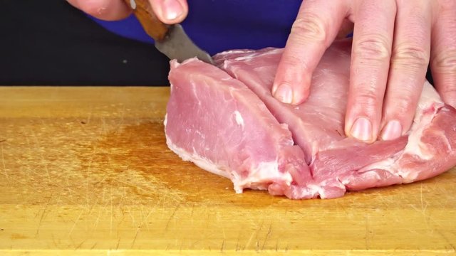 Person's Hands utting Piece of Raw Meat on Vintage Wooden Surface. Chef Man Holding Knife With Hands And Cutting . Cutting Meat on a Wooden Kitchen Board