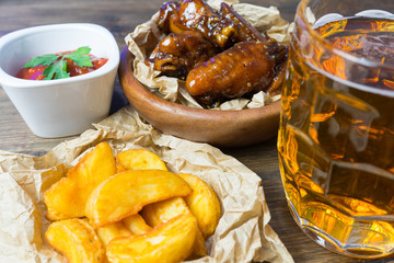 Chicken wings in a fragrant and pungent sauce with sesame seeds. A glass of fresh cold beer and fried potatoes with rustic tomato sauce from fresh tomatoes and herbs