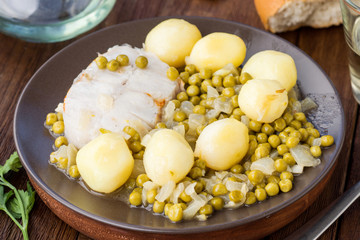 hake with stewed potatoes in green sauce and peas, on wood