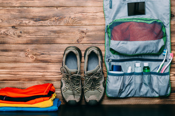 set of things for hiking and travel on wooden background. Items include trekking shoes, clothes and a set for hygiene