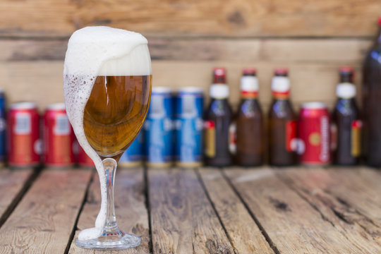 Copa de cerveza con espuma, latas y botellas de cervezas desenfocadas
