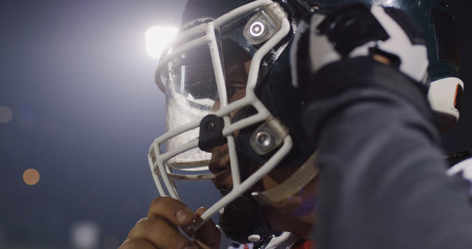 American Football Player Putting On Helmet on large stadium with lights in background