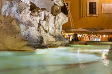 illuminated fountain in front of busy italian restaurant in a public square at night