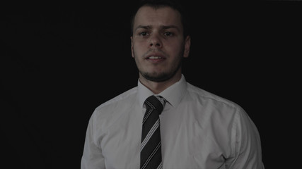 Handsome young businessman in white shirt, black background.