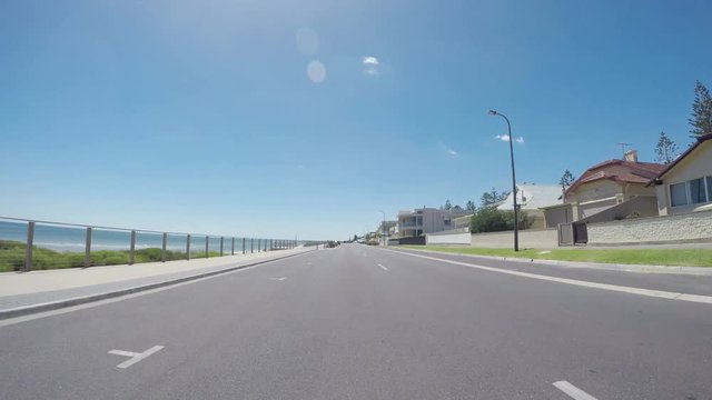 Vehicle POV, driving along The Esplanade, Henley Beach, South Australia, with views of ocean and beach, and homes overlooking the sea, time lapse.