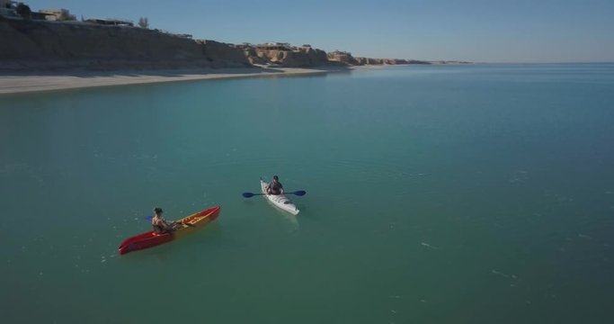 Aerial view of a couple kayaking in a sea toward a mountain in the distance.