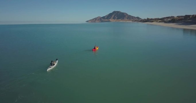 Aerial camera approaching and flying over two kayakers paddling toward a mountain.