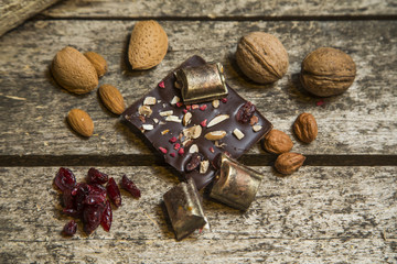 Pieces of black, chocolate with cranberry , nuts and almond  on wood background
