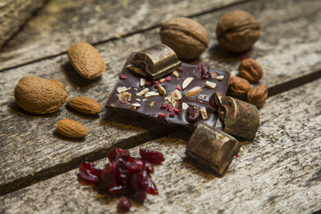 Pieces of black, chocolate with cranberry , nuts and almond  on wood background