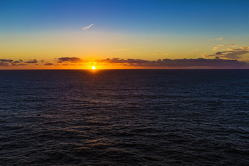 Sun setting on horizon between ocean and sky