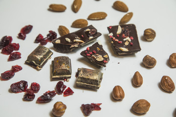 Pieces of black, chocolate with cranberry , nuts and almond  on white background.
