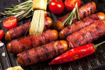 Festive cocktail sausages wrapped in crispy smoked bacon commonly known as 'Pigs in Blankets' in black pan