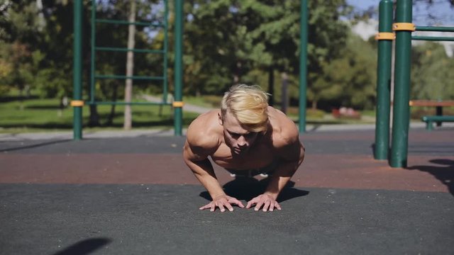Athletic young man doing push ups outside on sports playground